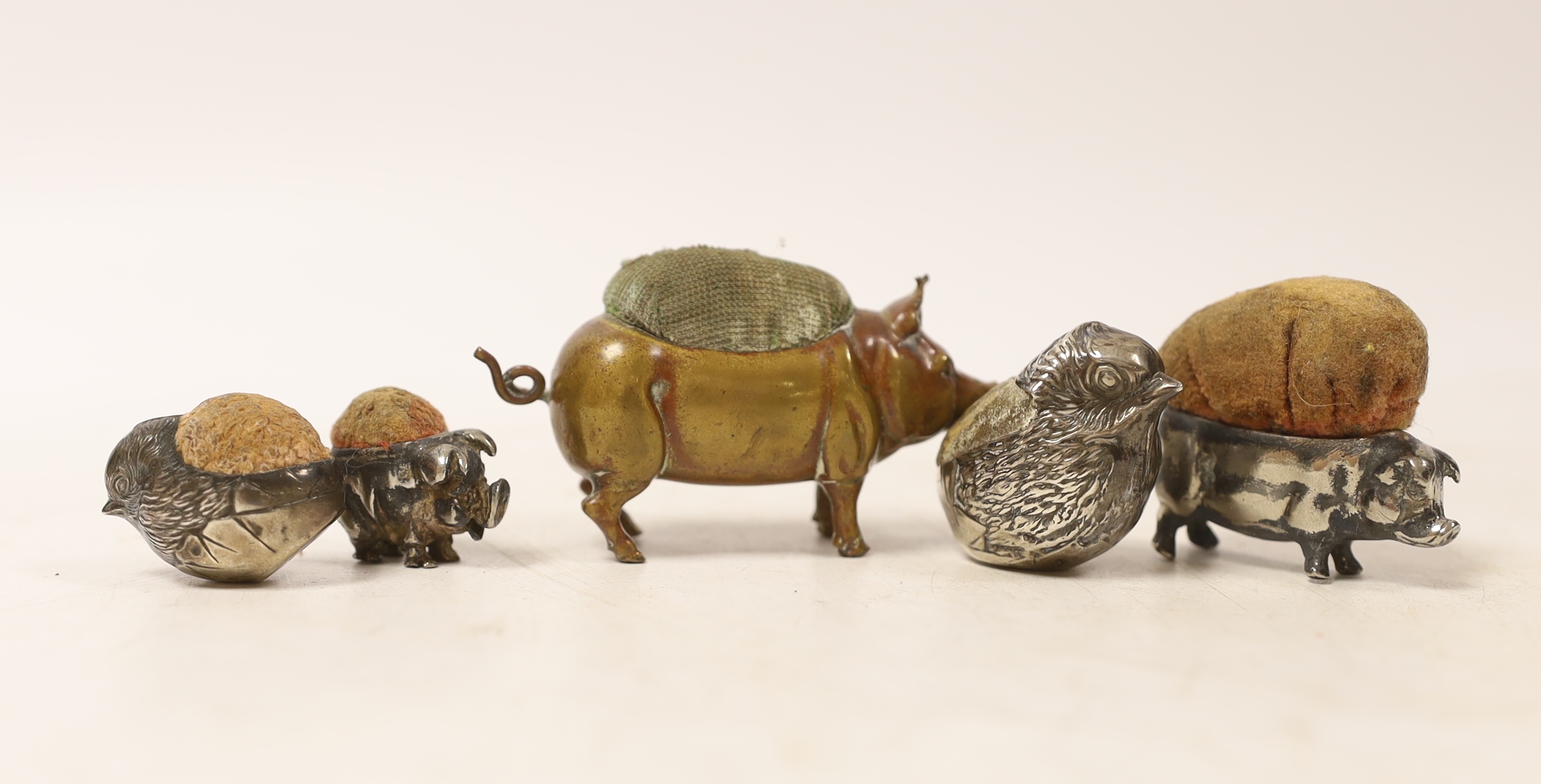 Two Edwardian silver mounted novelty pin cushions, modelled as hatching chicks, both by Sampson Mordan & Co, 1907 & 1909, largest height 33mm, together with three base metal mounted pin cushions.